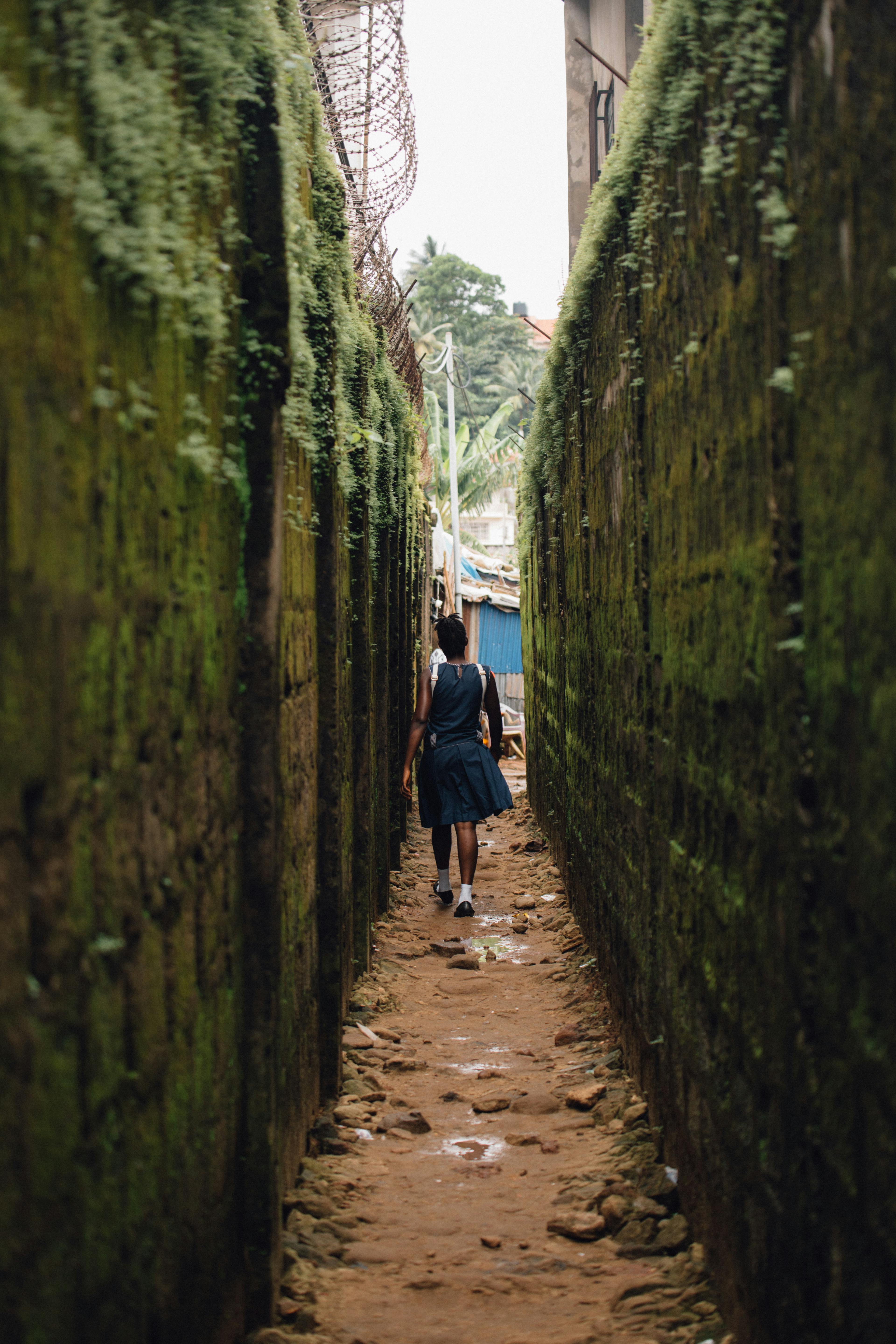 白天，一个女人穿过一条狭窄、苔藓覆盖的小巷，传达出探索和冒险的感觉