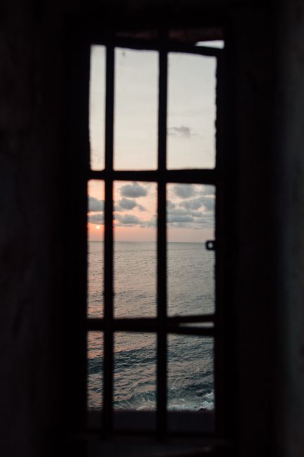 Dramatic ocean view with a sunset framed through window bars, evoking a sense of freedom.