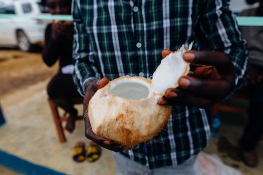 Close-up of a man holding an open coconut with water inside, outdoors, showcasing a refreshing tropical drink.