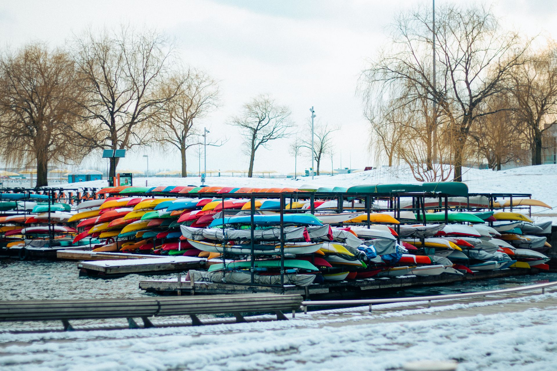 Vibrant kayaks stacked by a snowy waterfront in Toronto, Canada during winter.
