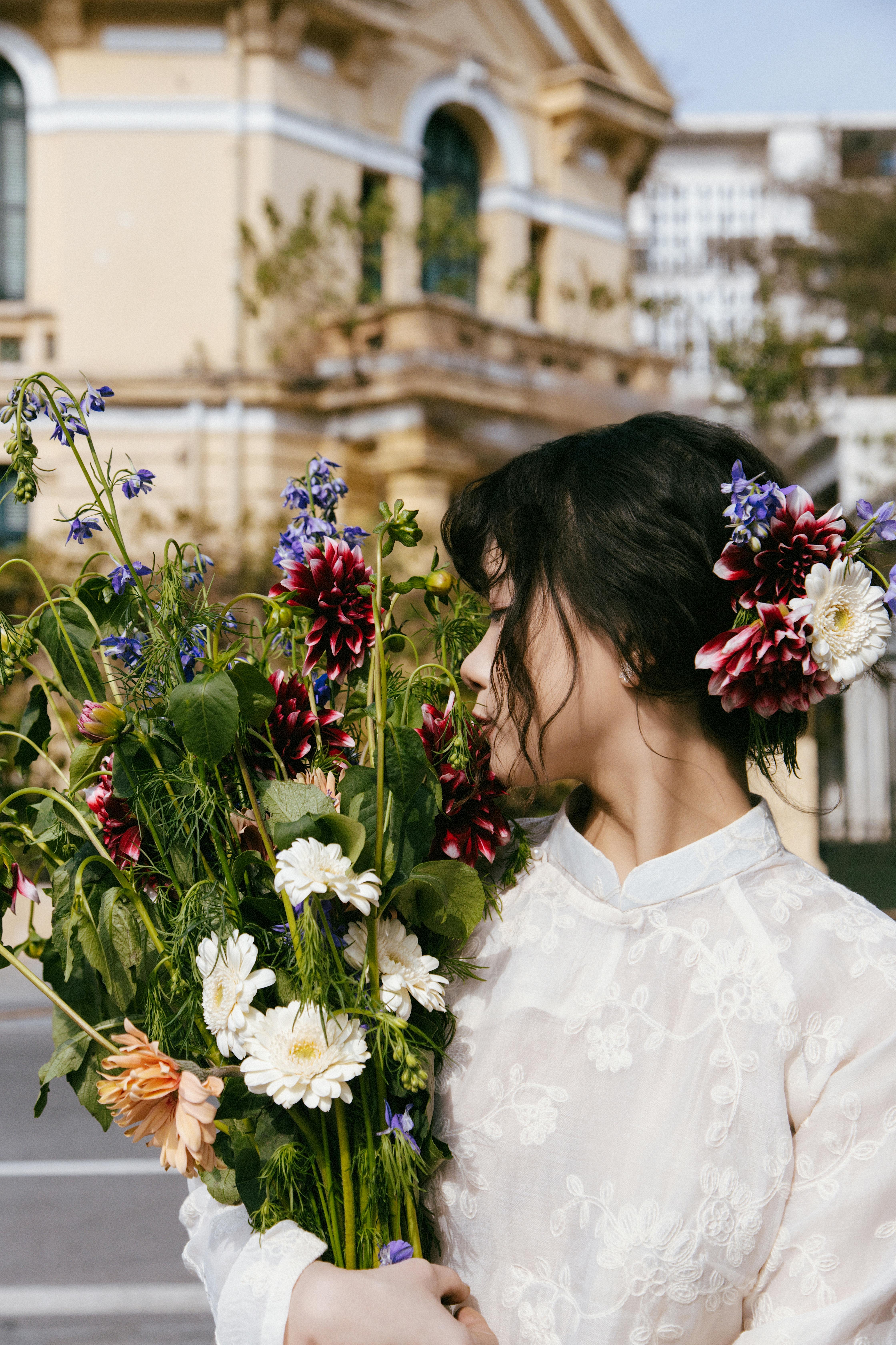 A young woman in traditional attire holds a colorful bouquet outdoors in Hanoi, Vietnam.