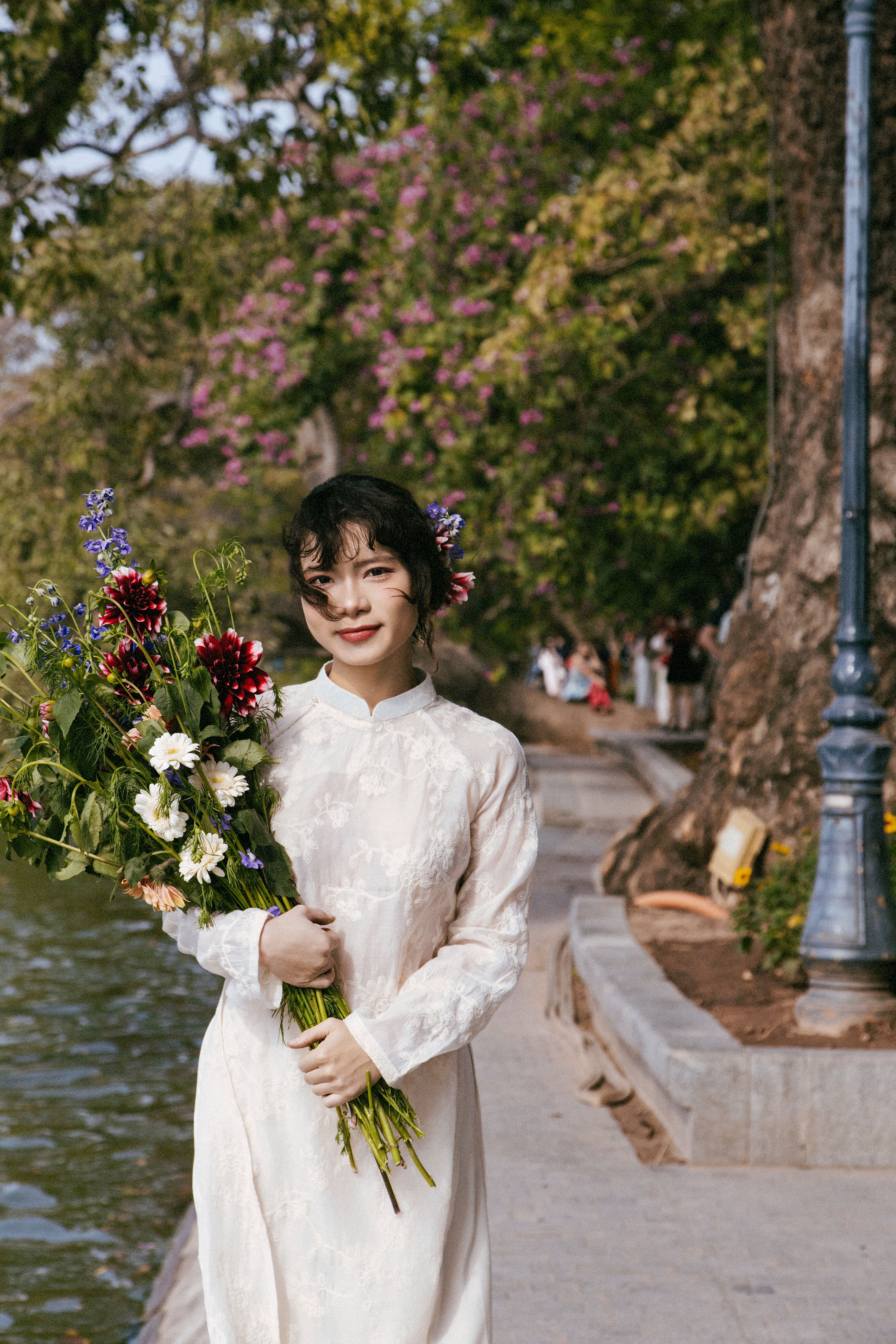 A woman in traditional dress holding flowers by a serene lake in Hanoi, Vietnam.