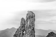 冒险的登山者登上了高耸的岩石山峰顶峰，天空阴沉