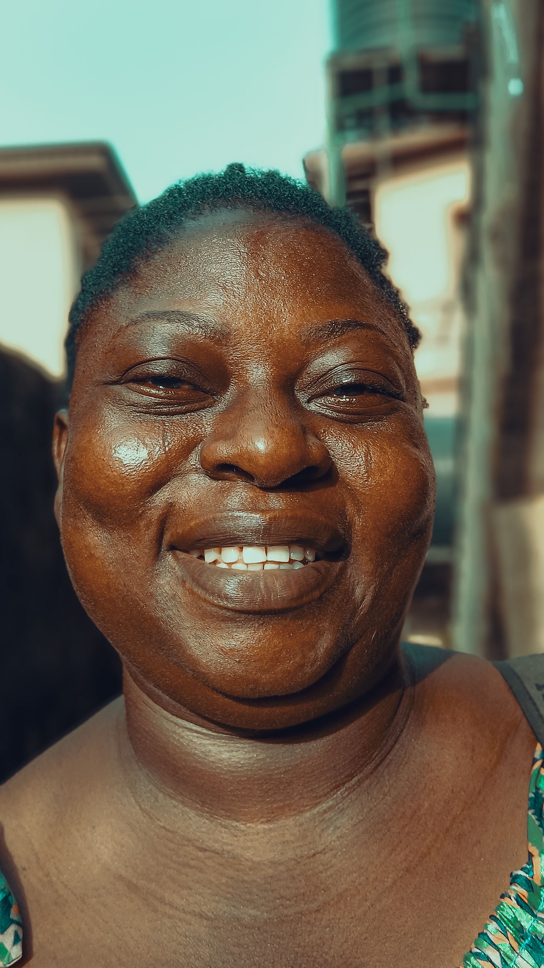A cheerful African woman smiles warmly in an outdoor rural setting, embracing happiness.