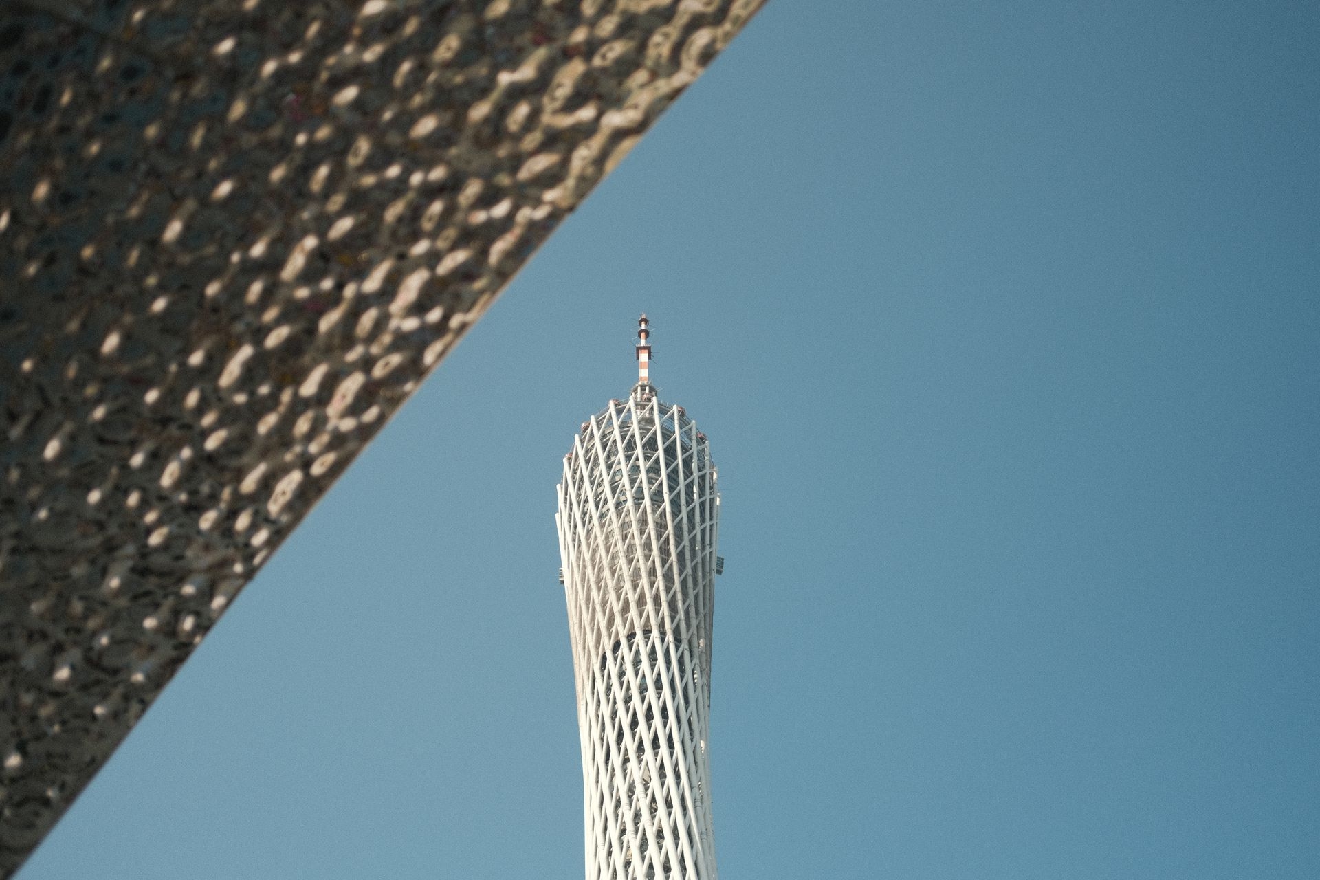 A striking view of the Canton Tower framed by architecture against a clear blue sky.