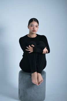 Young woman sitting on a stool in black attire, showcasing a minimalist aesthetic.