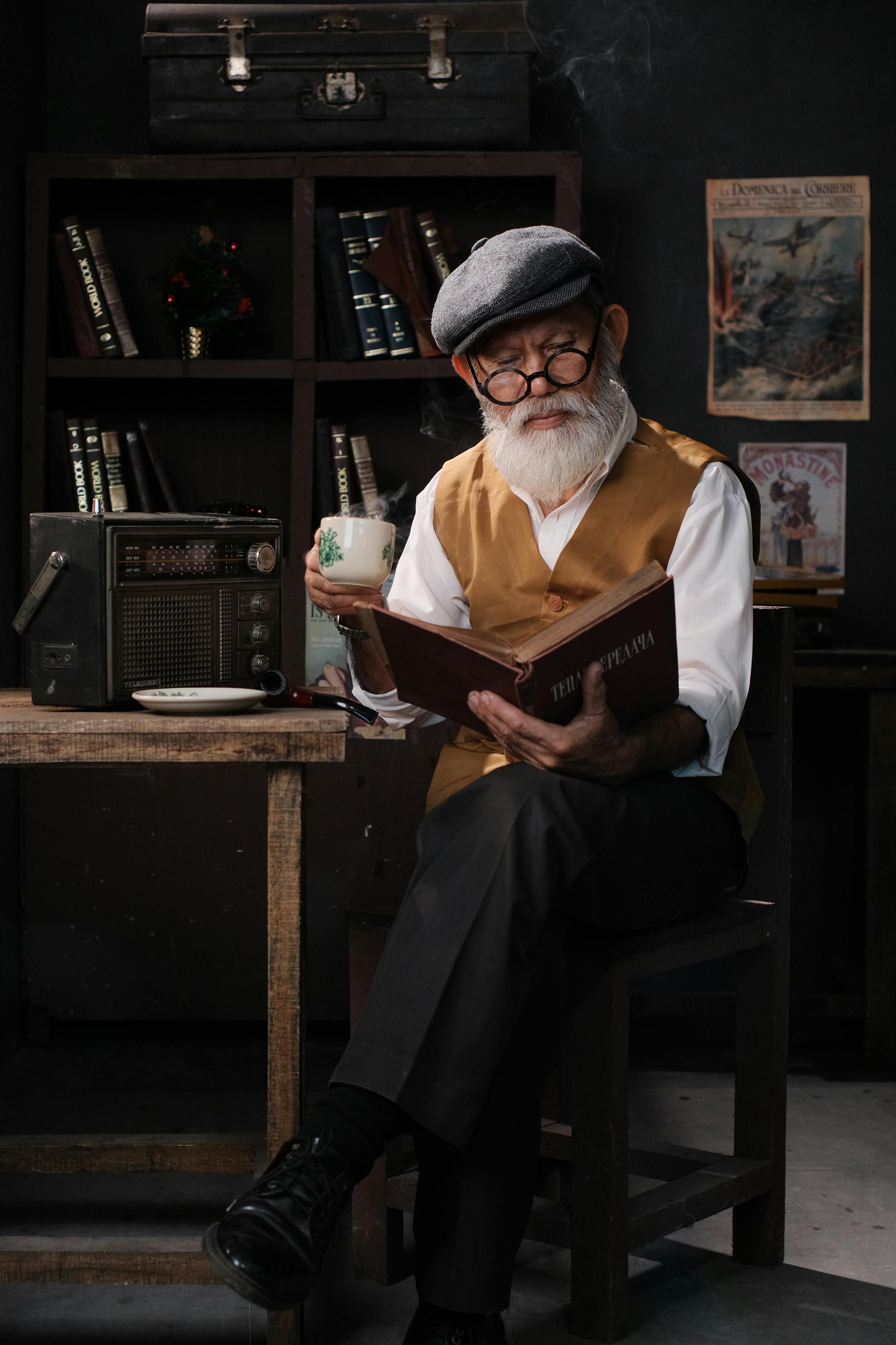 Senior man with book and cup in a vintage study setting, showcasing a nostalgic atmosphere.