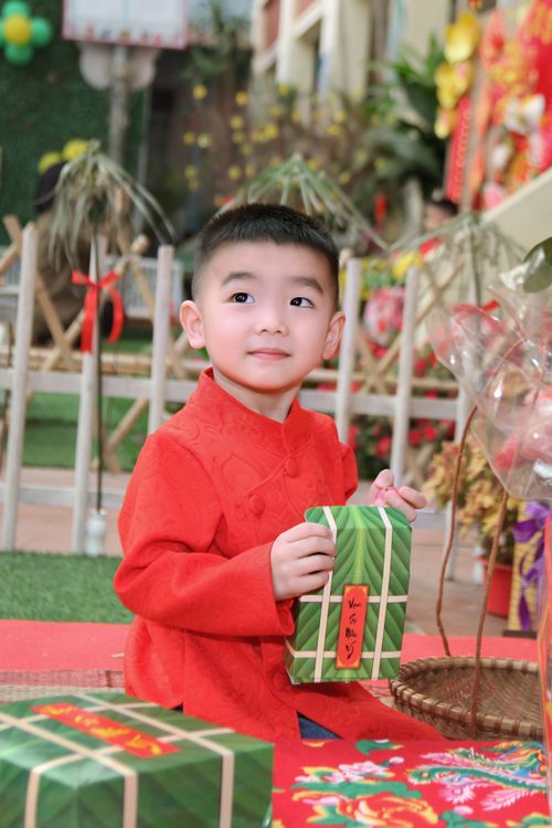 Free A young boy in a red outfit holds a gift during a vibrant Lunar New Year celebration. Stock Photo