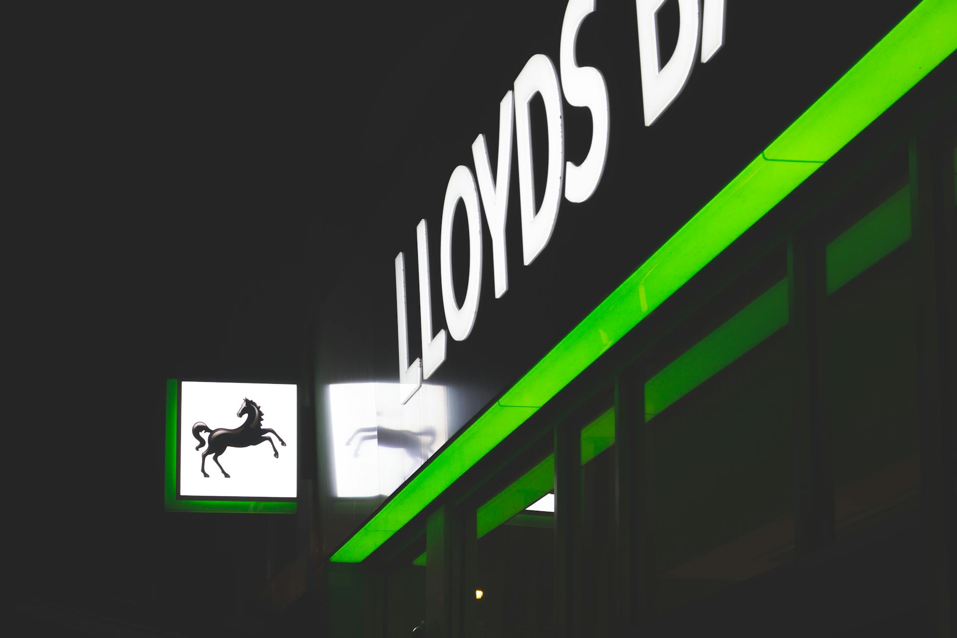 Bright green and white neon signs of Lloyds Bank against a dark night sky.