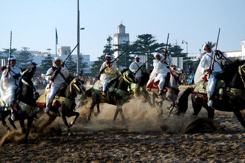 Free Cavalrymen in traditional attire perform a fantasia in Essaouira, Morocco, showcasing skilled horsemanship. Stock Photo