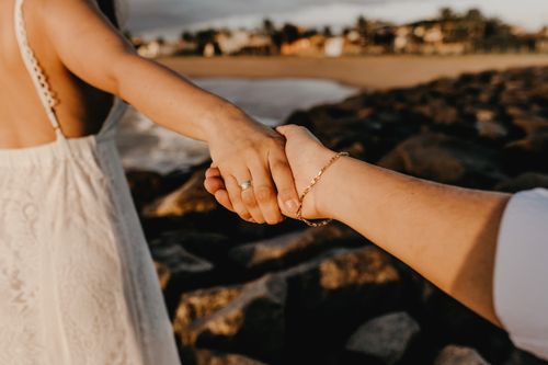 Free A romantic moment with a couple holding hands on a rocky beach at sunset. Stock Photo