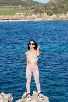 Woman in stylish activewear engaging in fitness by a scenic rocky seaside, promoting a healthy lifestyle.