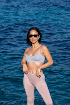 Confident woman in stylish activewear posing by the ocean, illustrating fitness and fashion.