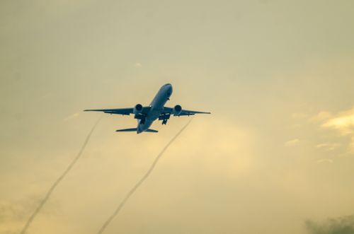 Free A commercial airplane ascending through a cloudy sky at sunset, leaving vapor trails. Stock Photo