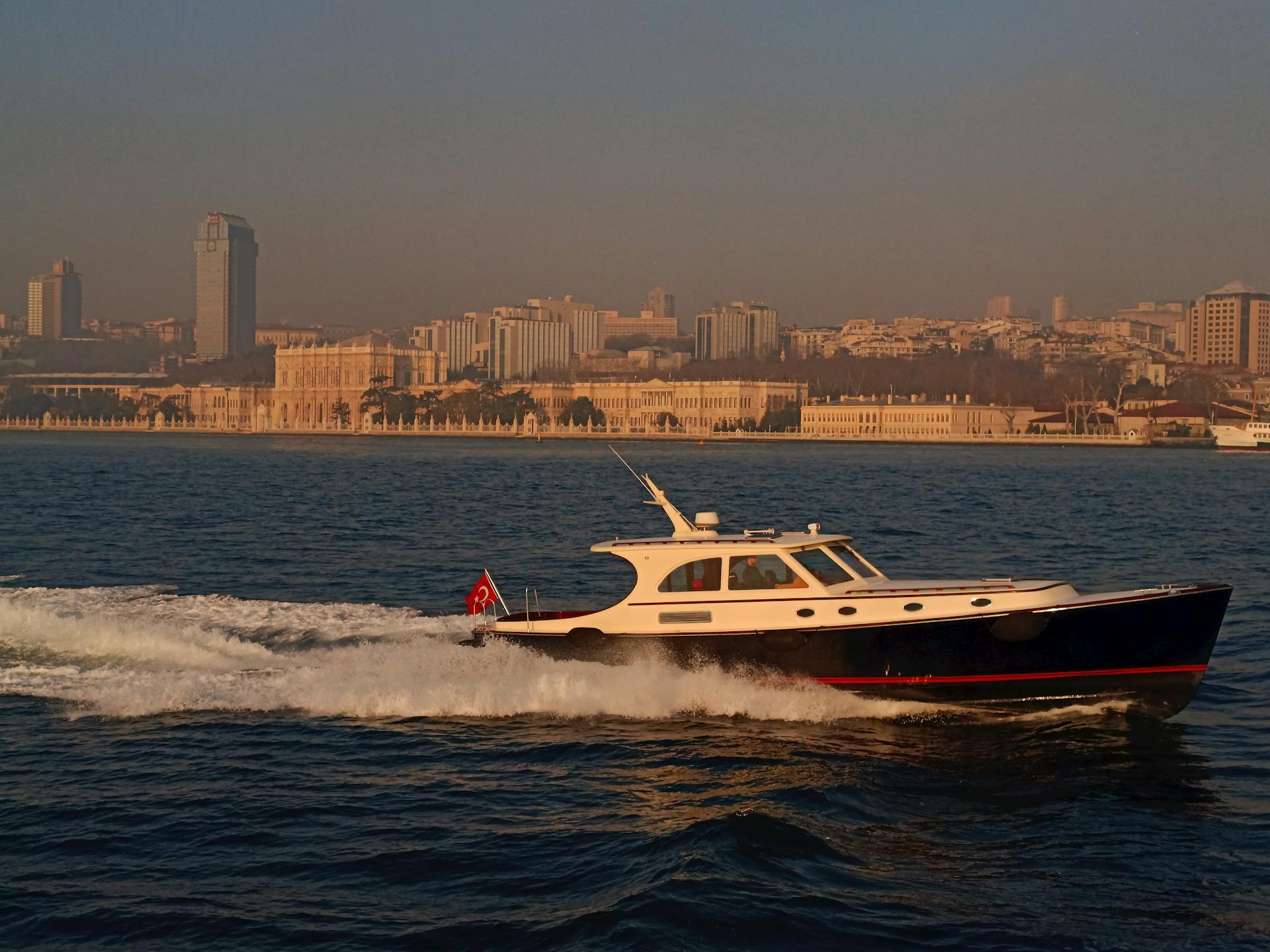 A luxury yacht sails past Istanbul's iconic waterfront at sunset, showcasing the city's skyline.