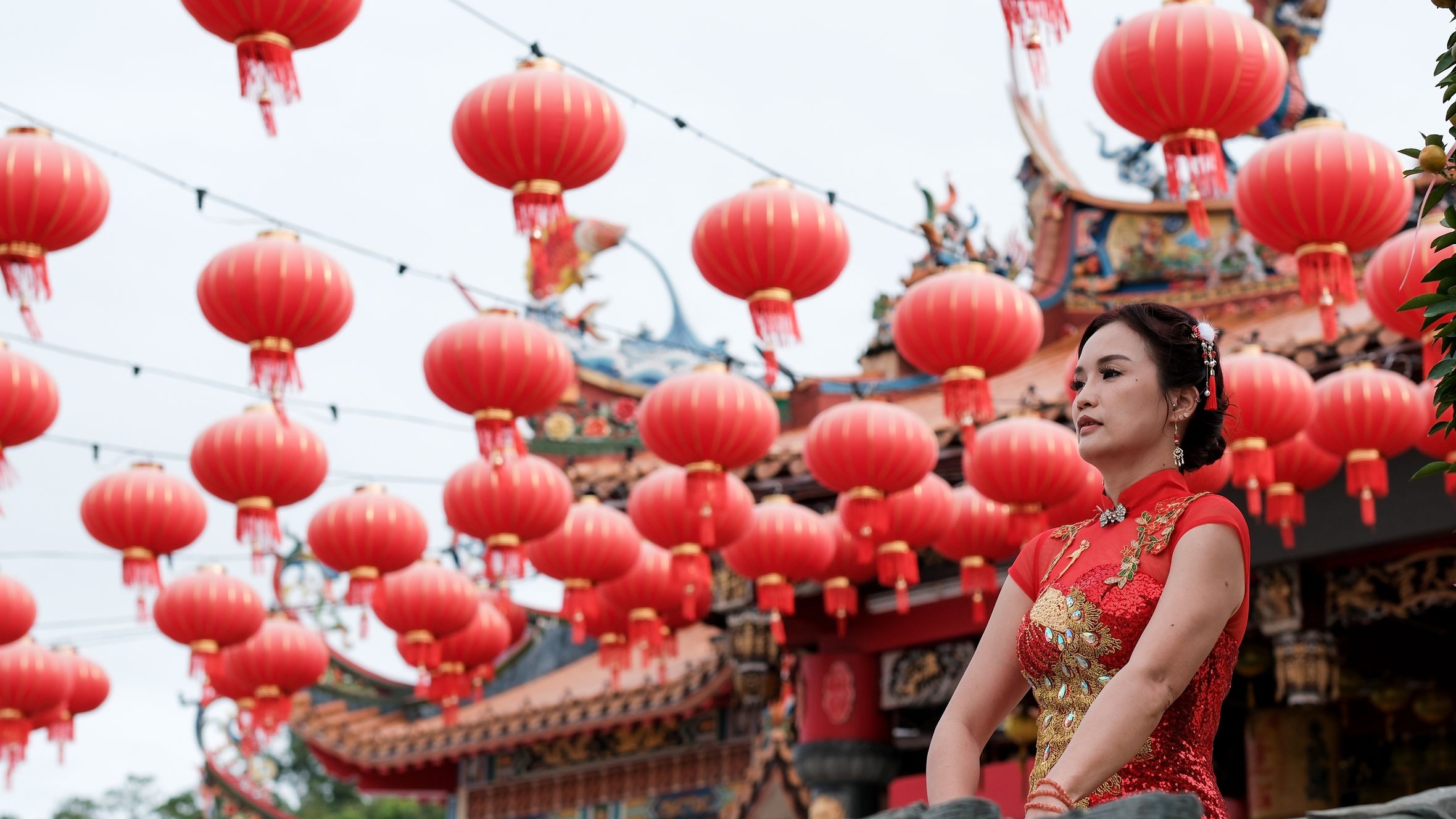 Woman in red qipao at a Chinese New Year lantern festival outdoors.