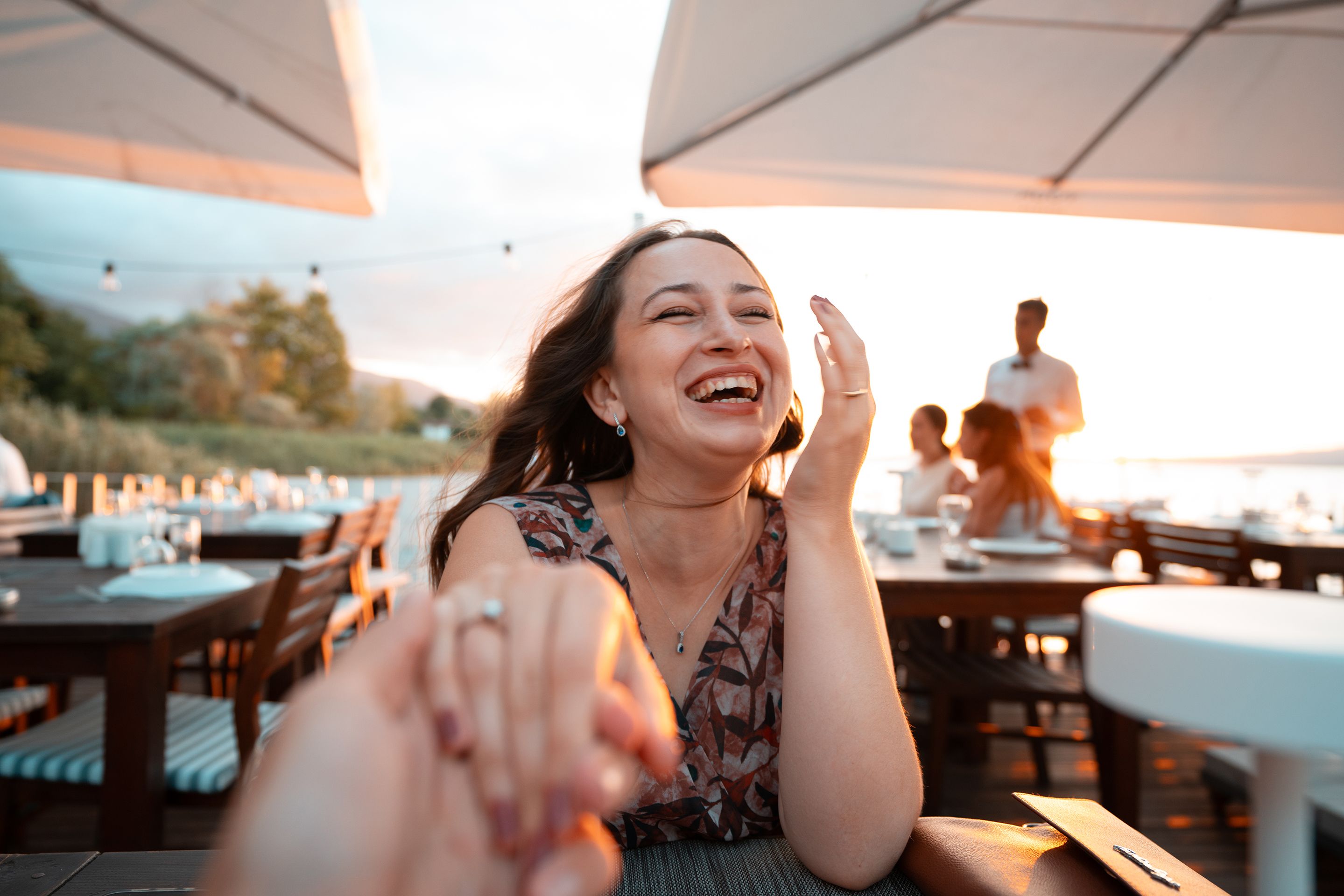 A woman laughing joyfully at an outdoor restaurant during sunset, capturing genuine happiness.