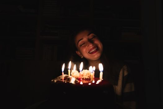 A joyful woman smiles at a cake lit with candles during her birthday celebration.