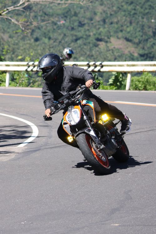 Free Motorcyclist in black gear taking sharp curve on sunny mountain road, showcasing dynamic movement and skill. Stock Photo