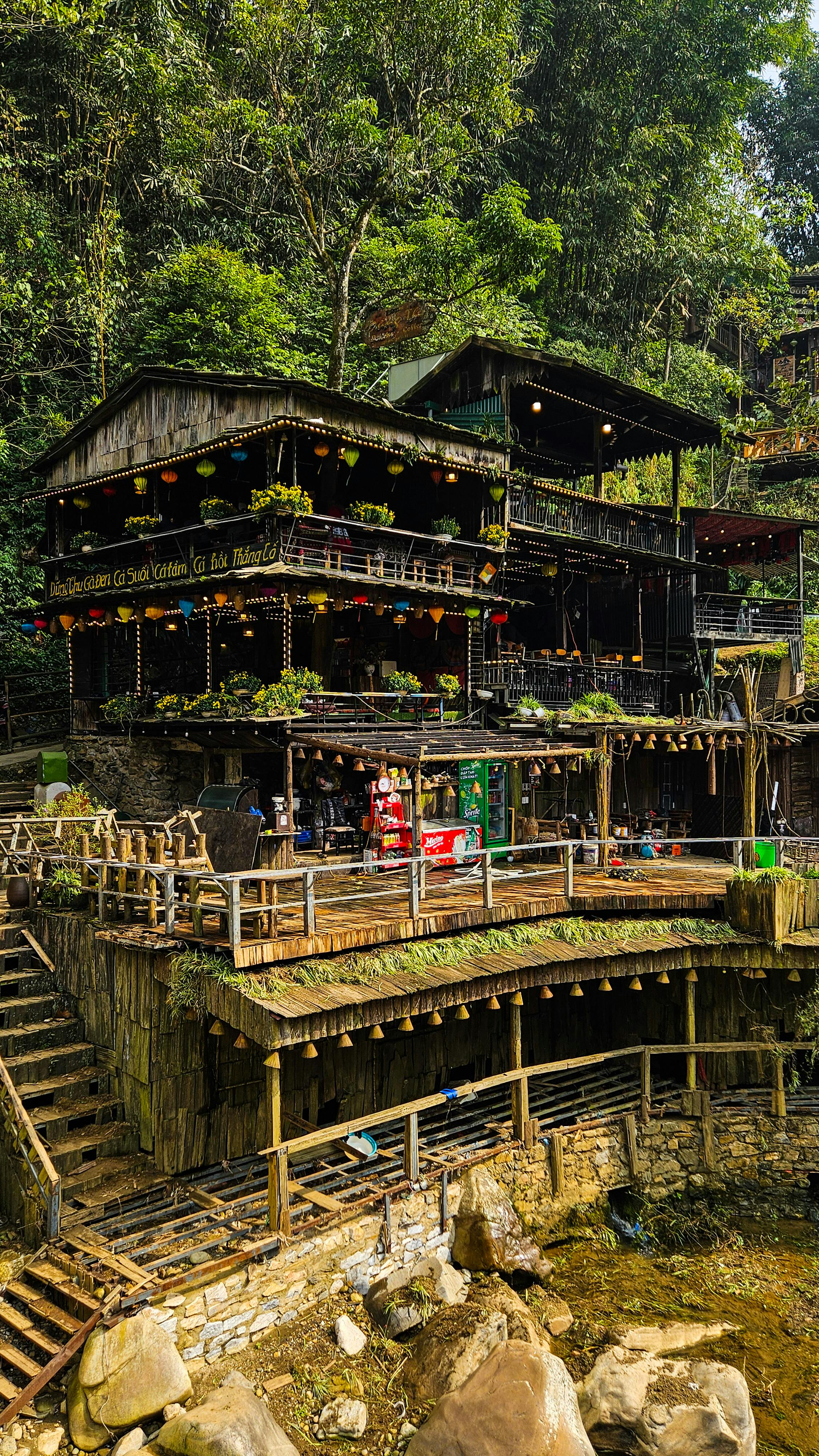 Charming rustic wooden restaurant nestled in lush green forest, featuring colorful decor and multi-level terraces.