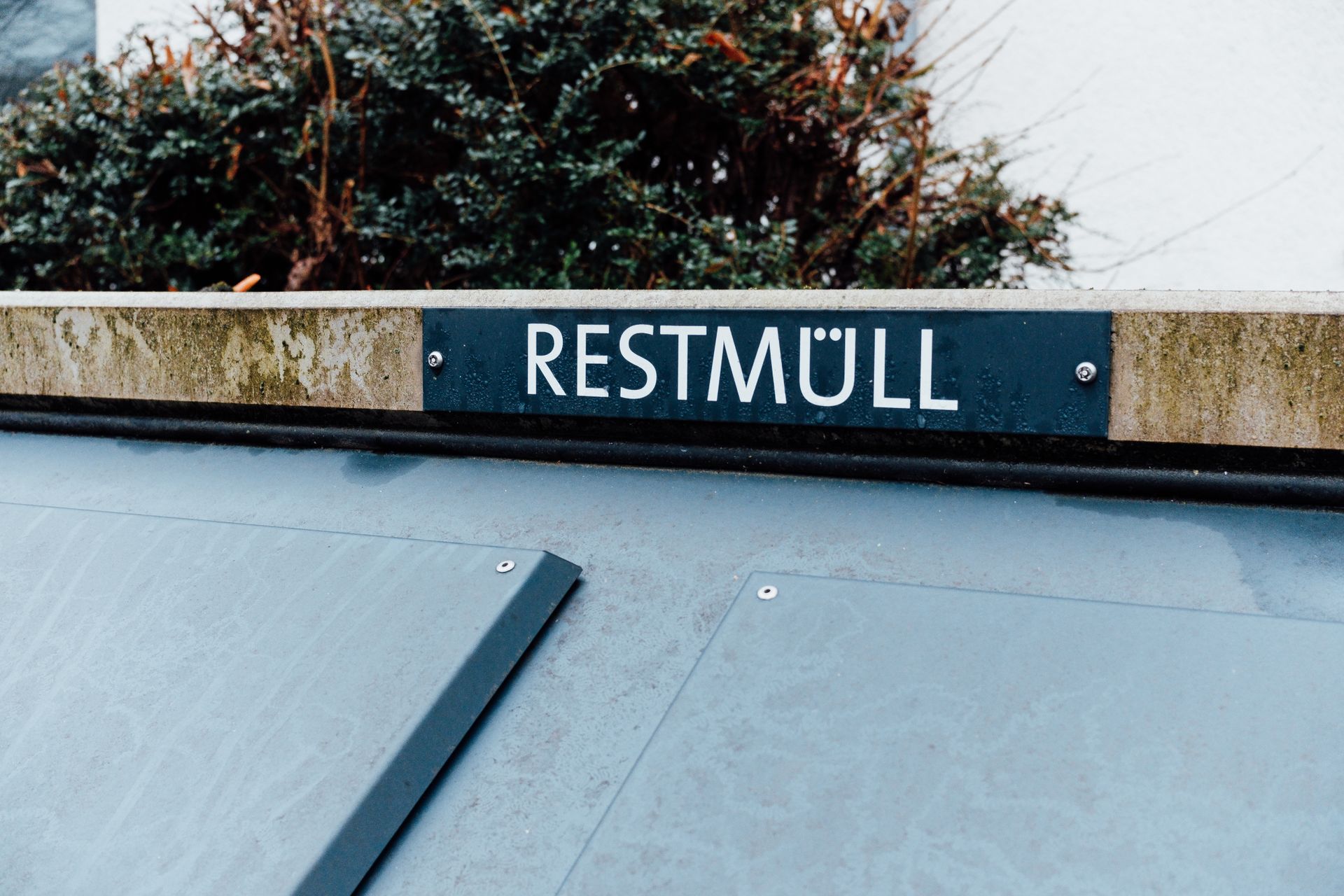 Photo of a Restmüll bin with a sign, against a backdrop of urban greenery.