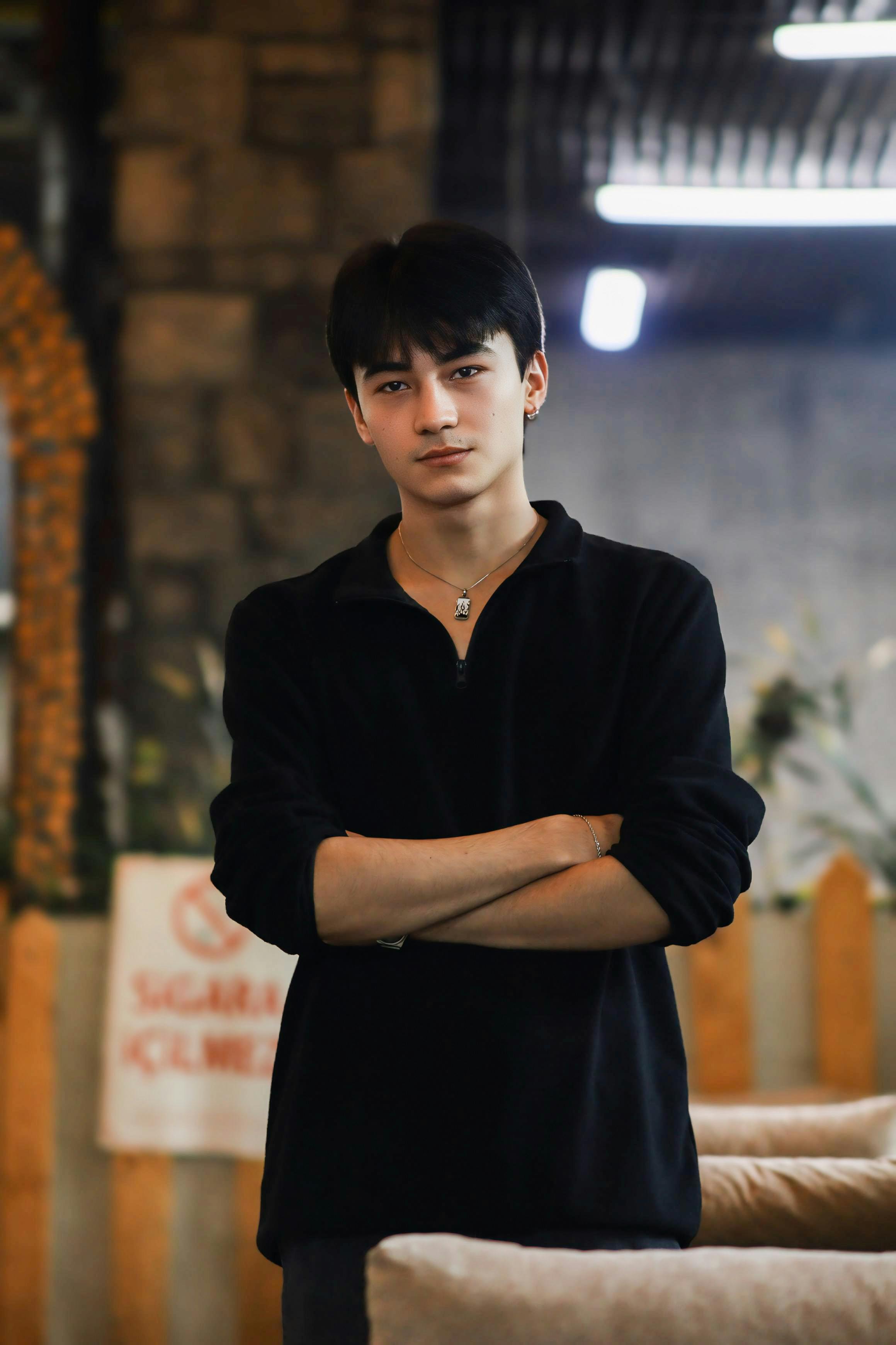 Portrait of a young man standing confidently indoors wearing a black sweater.
