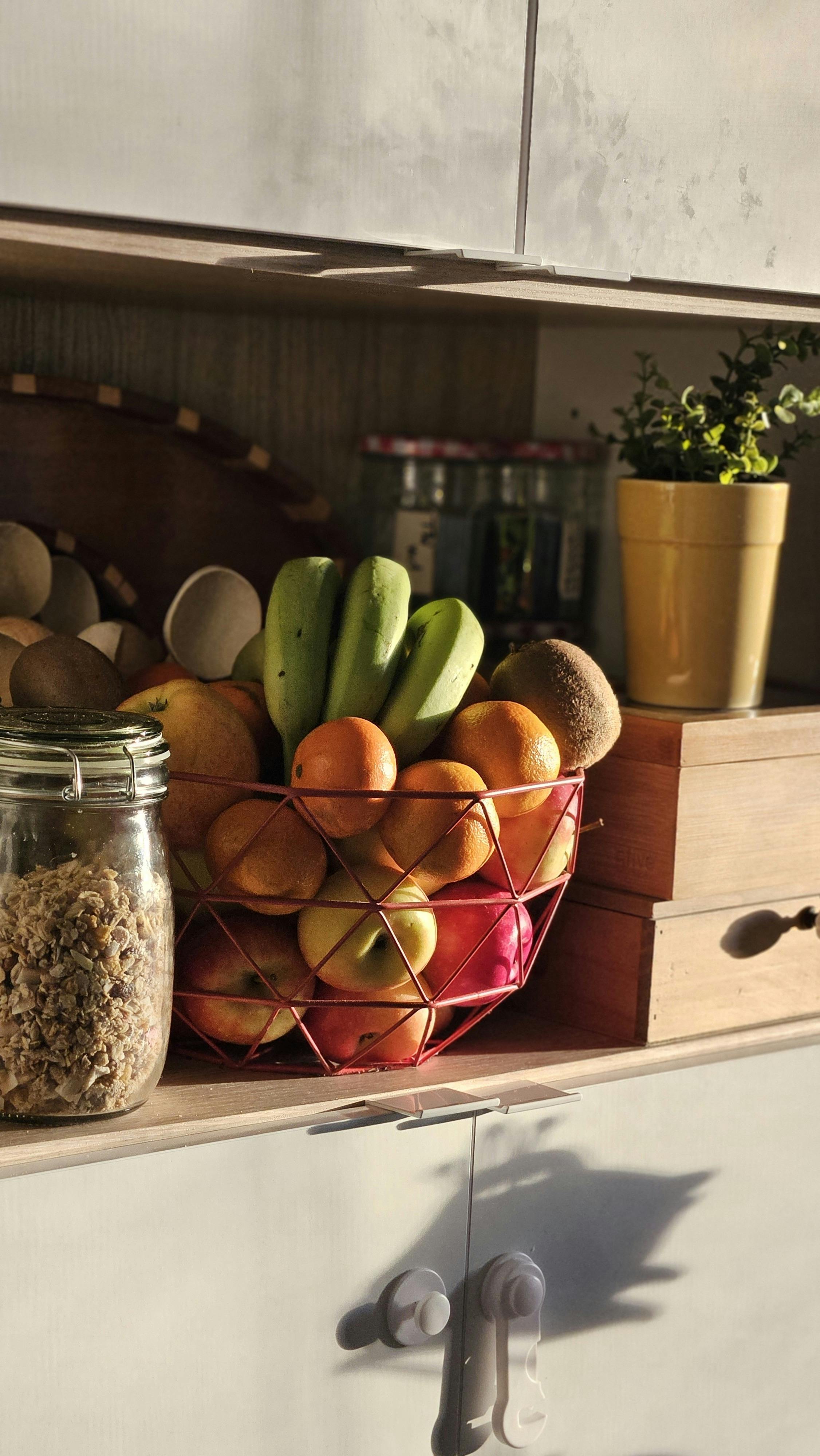 Sunlit kitchen scene featuring a variety of fresh fruits and a jar of granola.