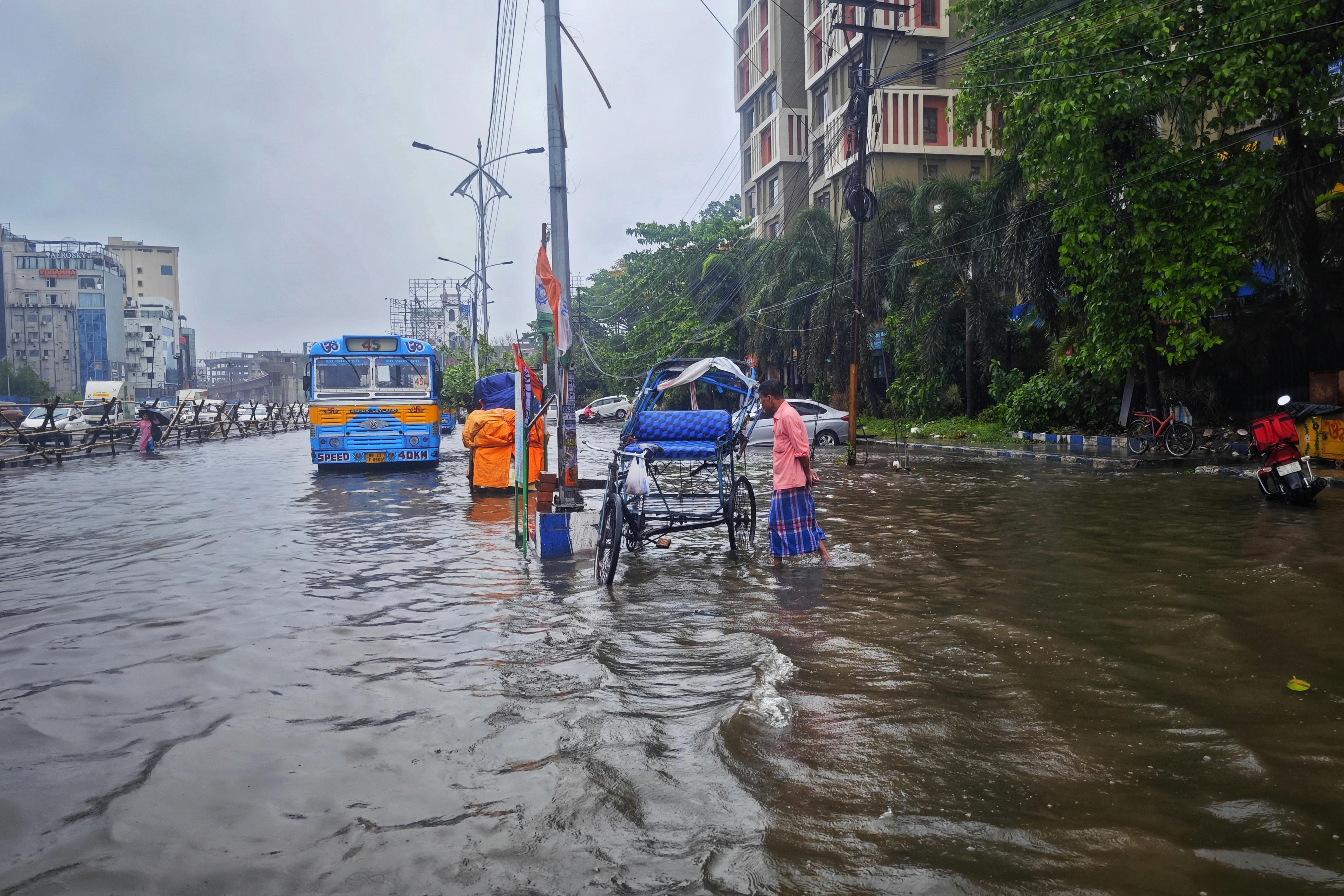 Street scene of monsoon flooding in Kolkata, India with vehicles and people navigating waterlogged roads.