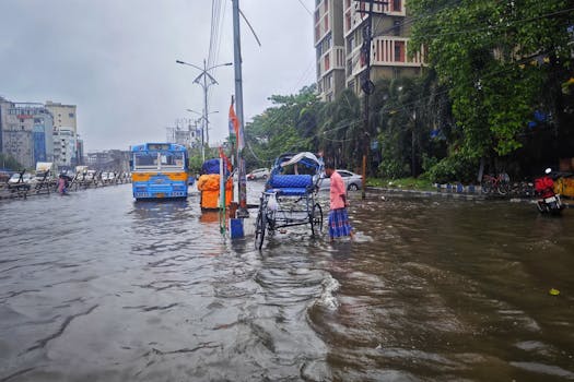 Street scene of monsoon flooding in Kolkata, India with vehicles and people navigating waterlogged roads.