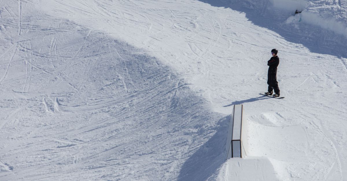 A snowboarder stands ready on a sunny slope in Laax snow park, Switzerland.