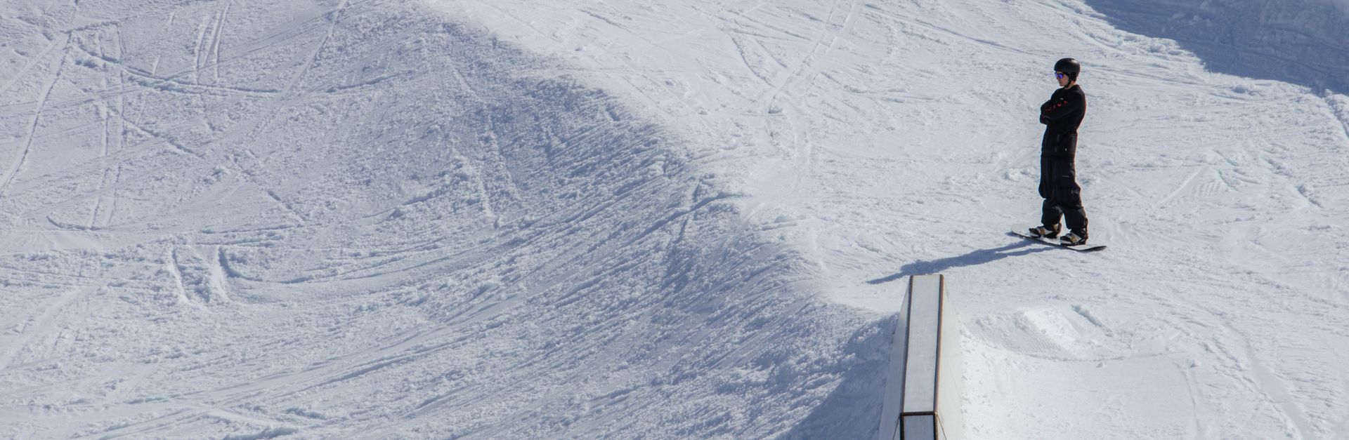 A snowboarder stands ready on a sunny slope in Laax snow park, Switzerland.