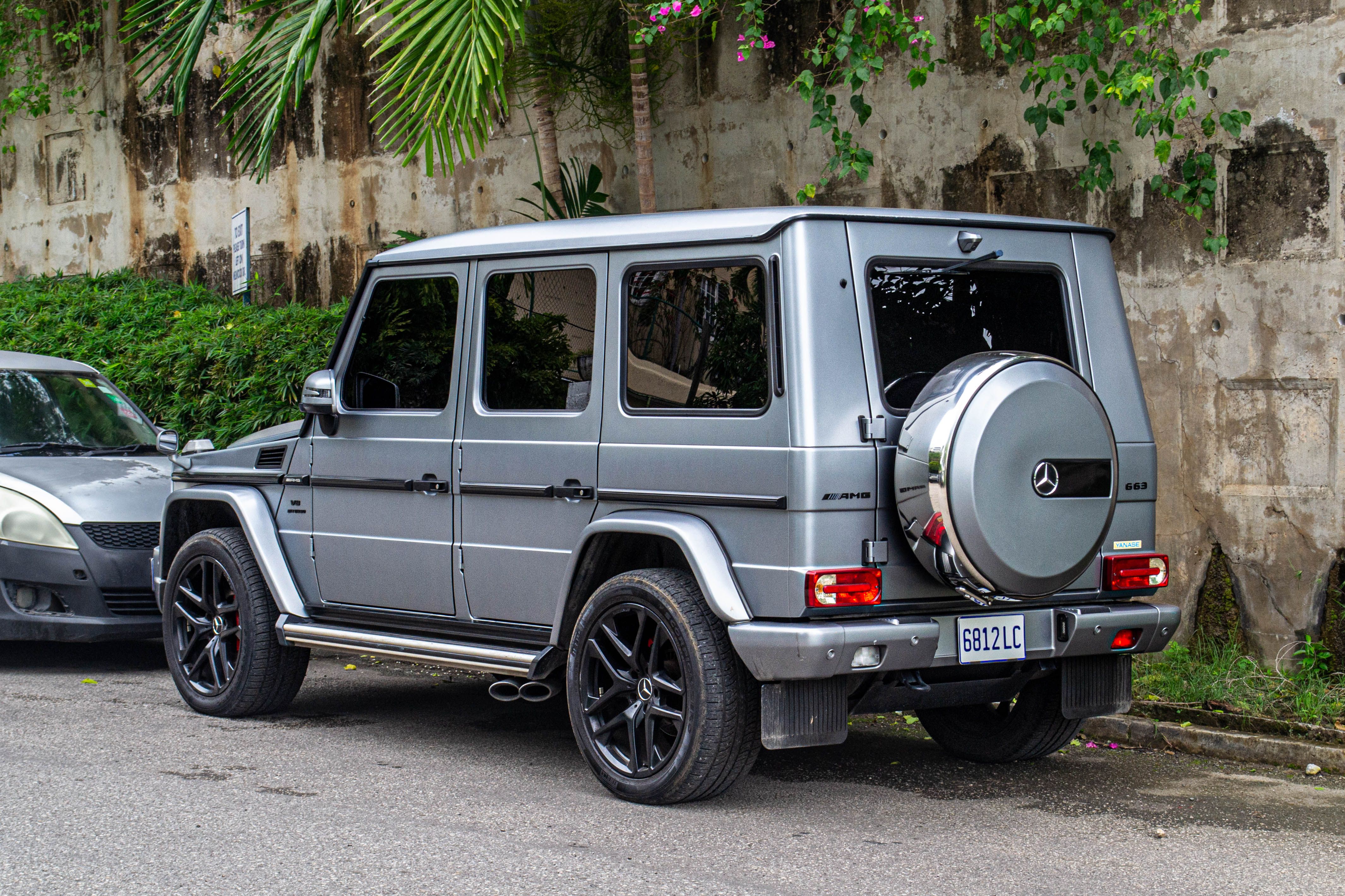 Silver luxury SUV with custom rims parked outdoors in scenic Jamaican street with lush green foliage.