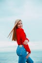 一位时尚的年轻女子身着红色上衣和牛仔裤，在海滨休闲时尚拍摄中摆出姿势