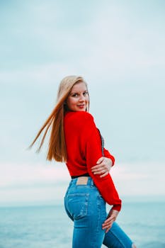 一位时尚的年轻女子身着红色上衣和牛仔裤，在海滨休闲时尚拍摄中摆出姿势