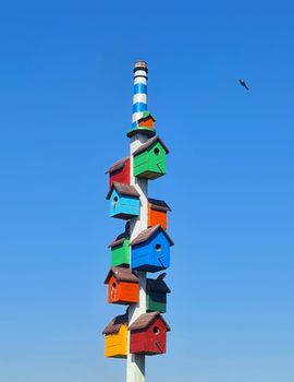 Vibrant birdhouses stacked on a pole against a clear blue sky, showcasing outdoor artistry.