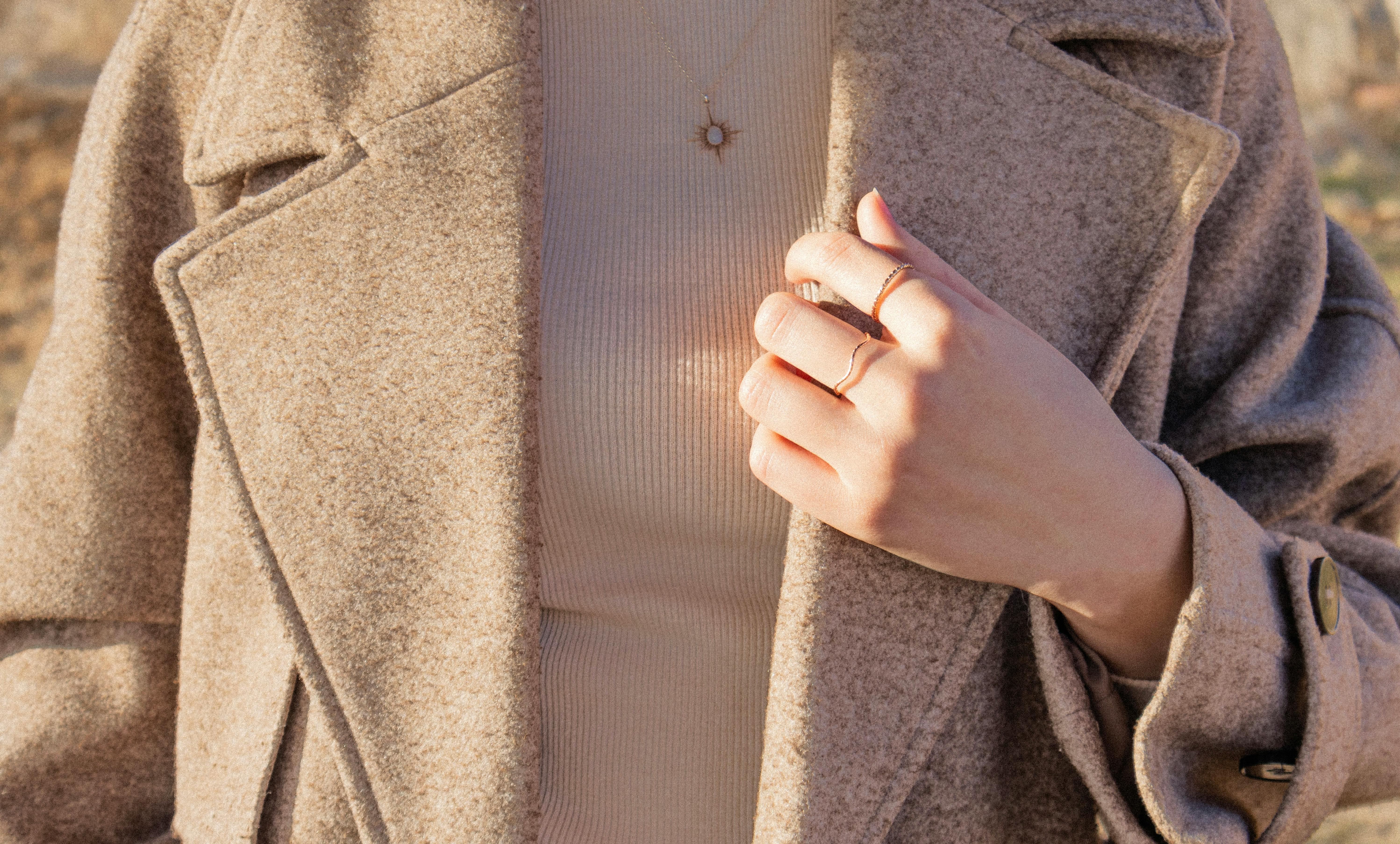 Close-up of a woman in a beige coat wearing elegant minimalist jewelry, showcasing fashion trends.