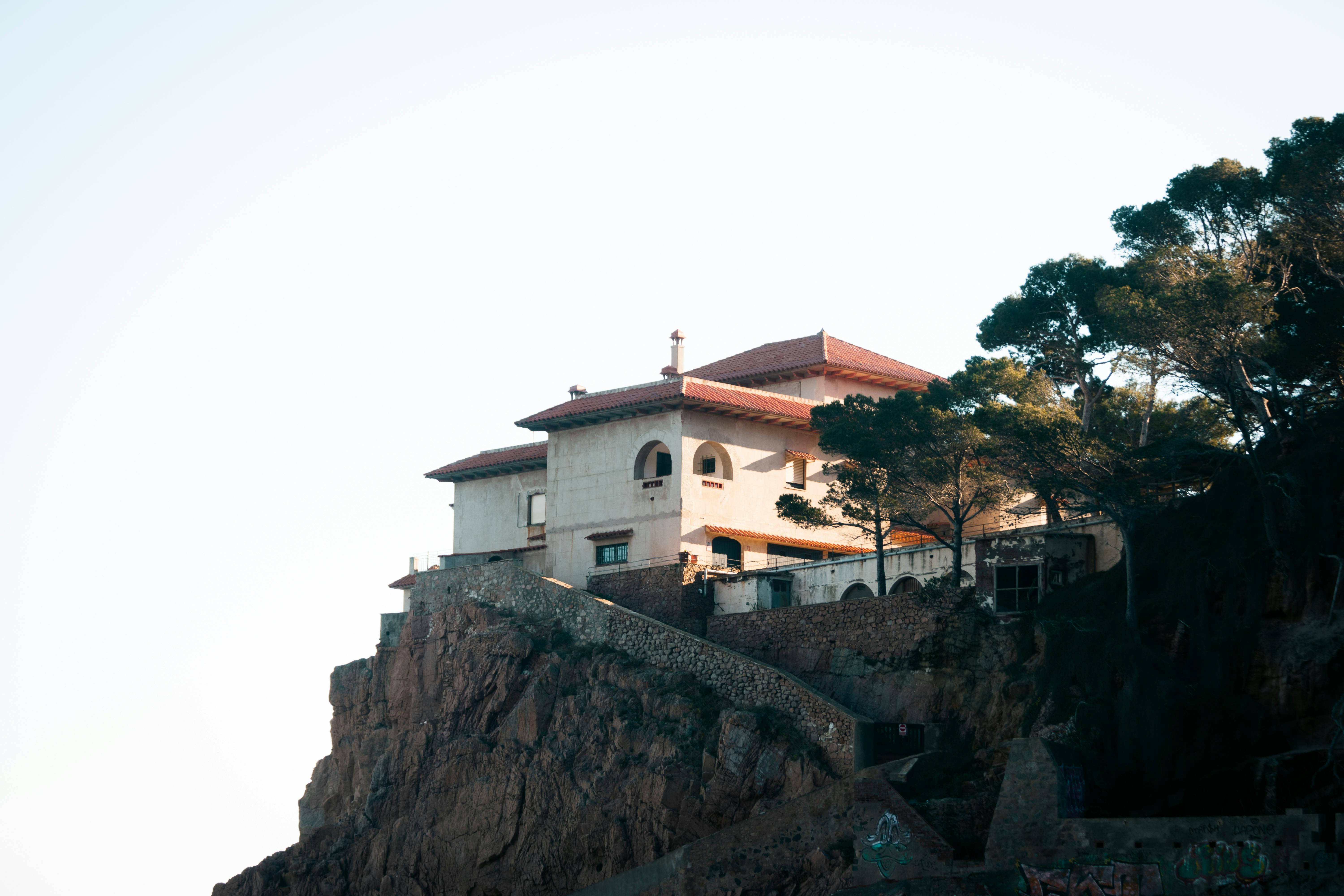 Elegant villa perched on a cliff in Costa Brava, framed by trees against a clear sky.