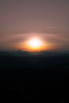 A serene view of the sun setting over a distant mountain range, casting warm hues.
