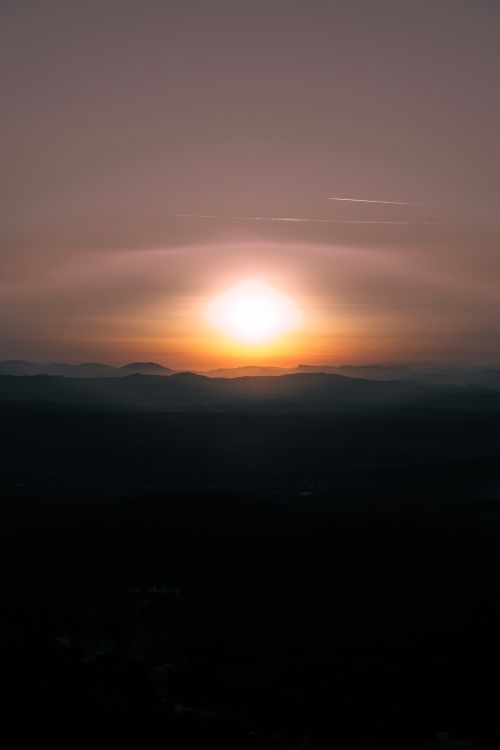 Free A serene view of the sun setting over a distant mountain range, casting warm hues. Stock Photo