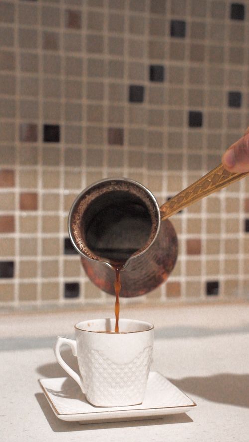 Free A copper pot pours hot Turkish coffee into a decorative white cup on a kitchen counter. Stock Photo