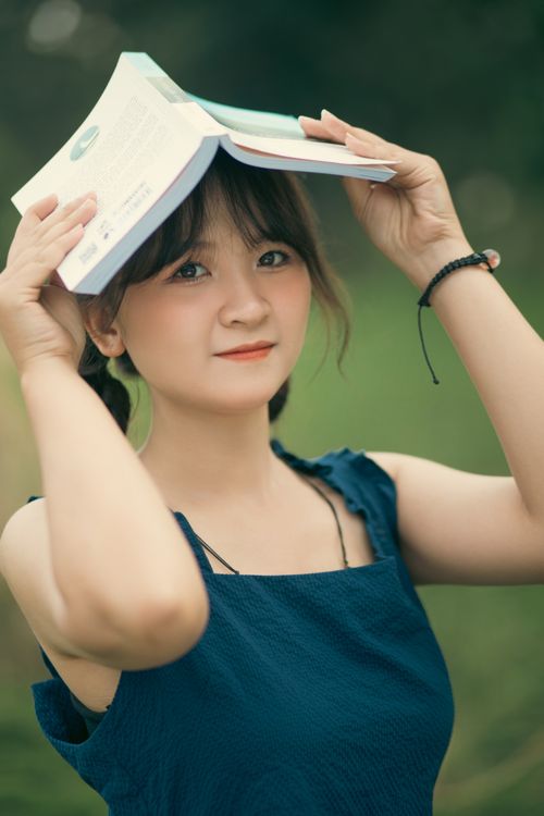 Free Portrait of a young woman holding a book outdoors with a summer vibe. Stock Photo