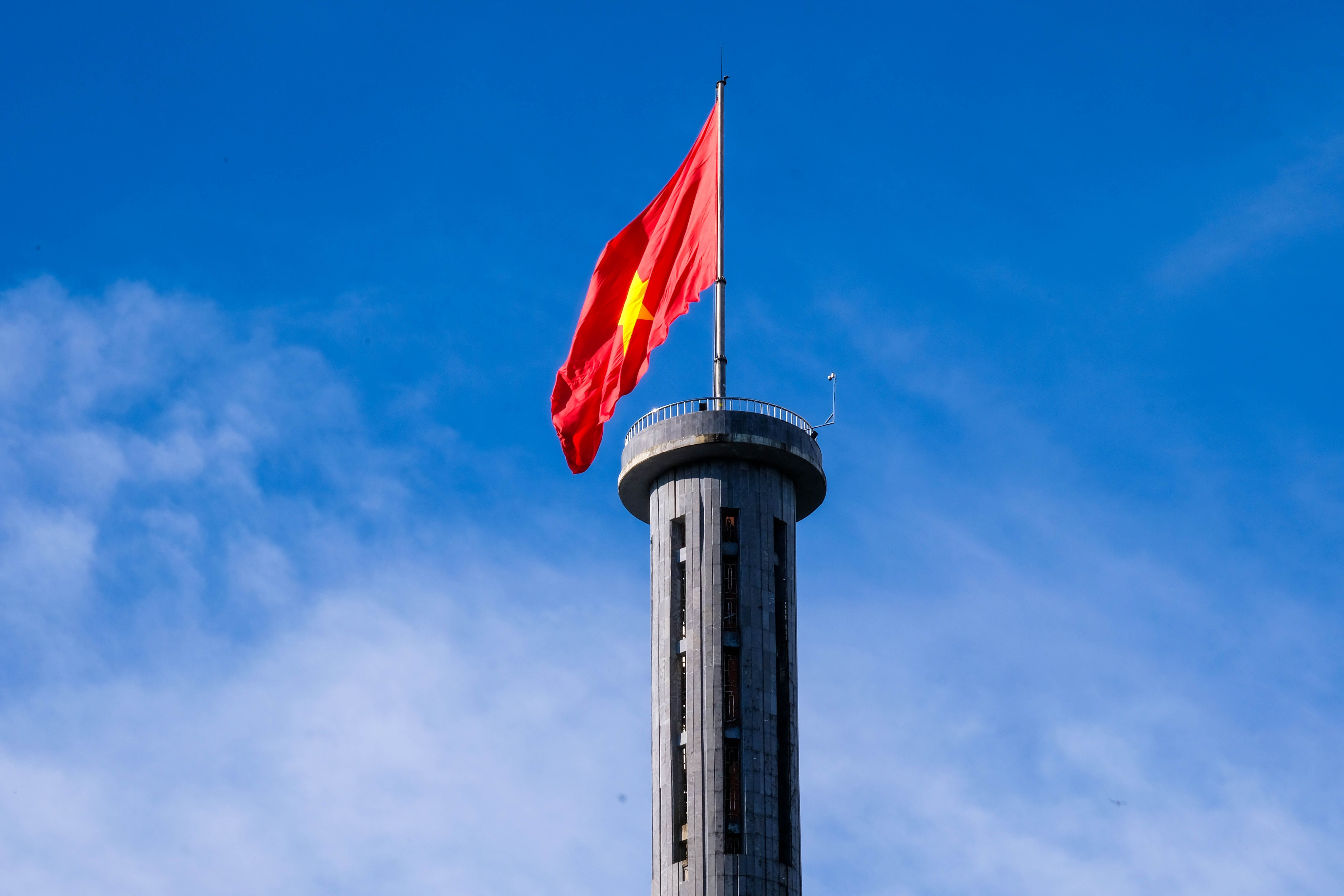 The Vietnamese flag flying from the viewing platform at the top of the Lung Cu Flag Tower against a blue sky