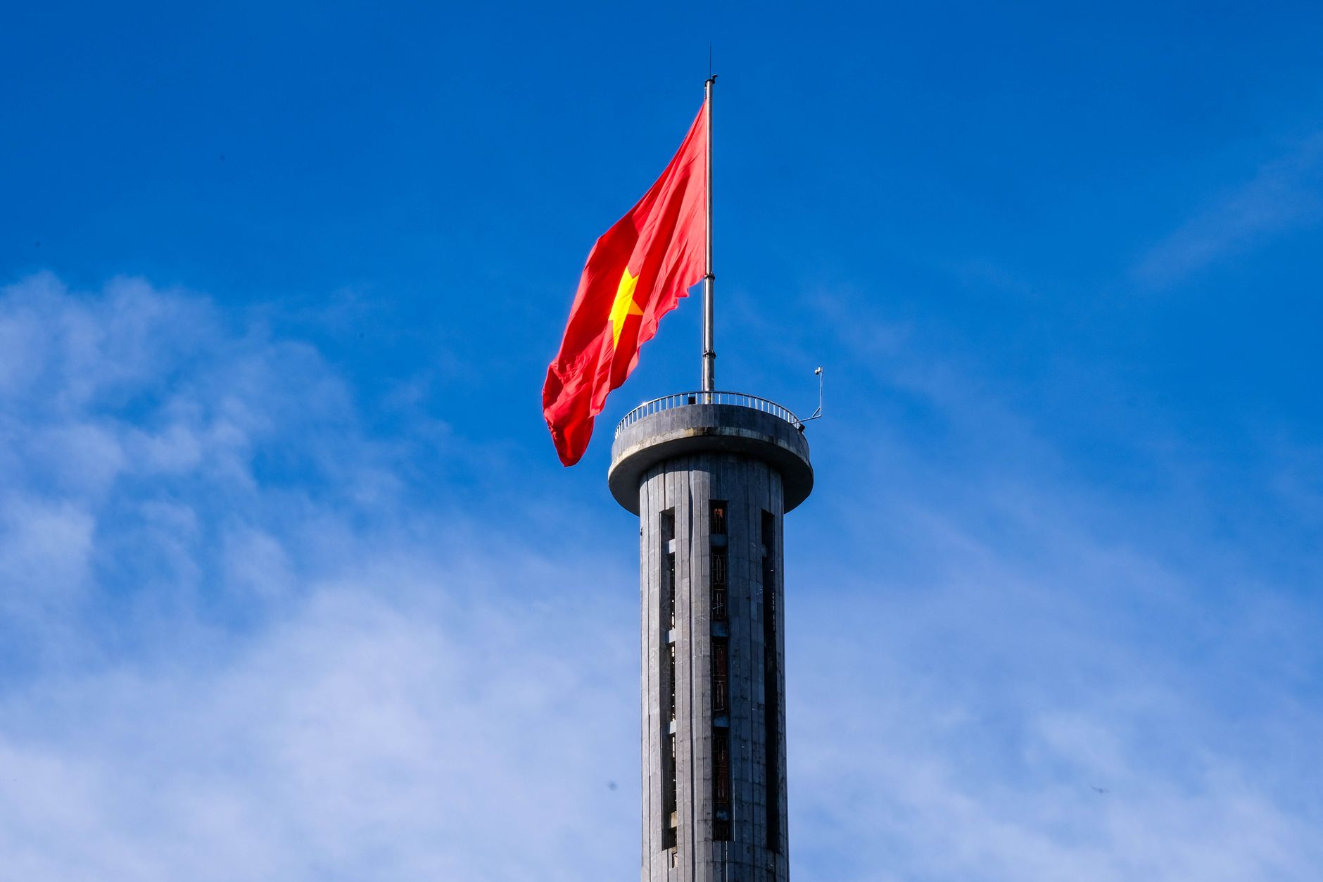 The Vietnamese flag flying from the viewing platform at the top of the Lung Cu Flag Tower against a blue sky