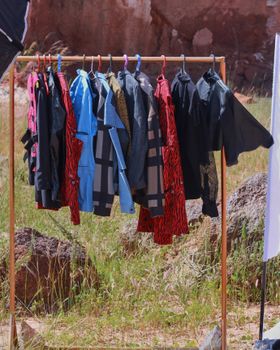 A selection of vibrant shirts hanging on a rack outdoors under sunlight.