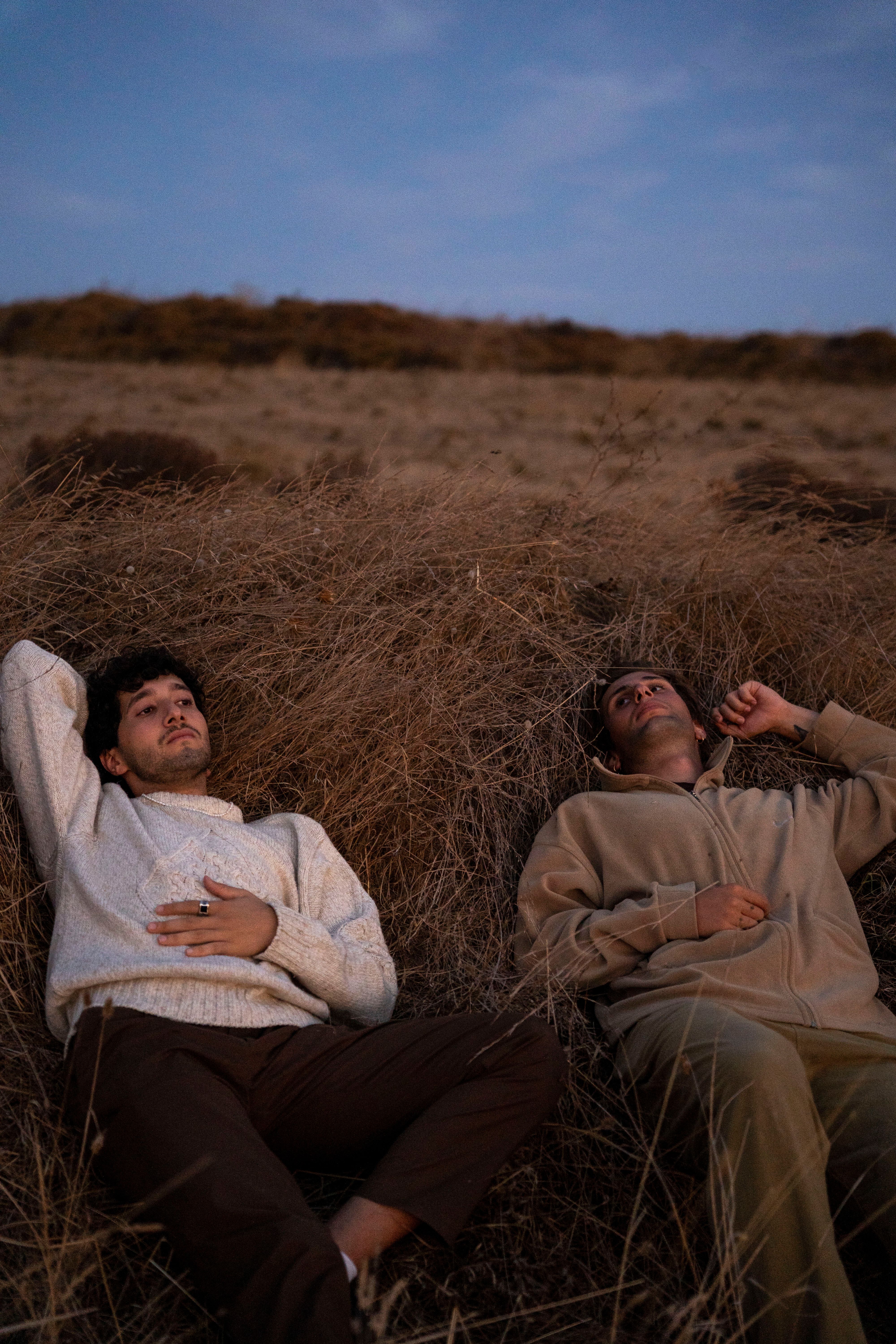 Two adults relaxing on a grassy hill during a serene autumn evening.