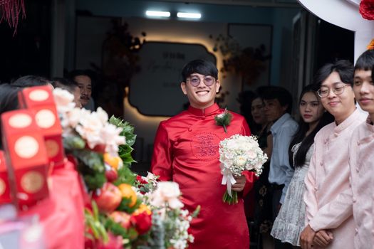 A joyful moment at an Asian wedding ceremony with the groom holding a bouquet, surrounded by guests.