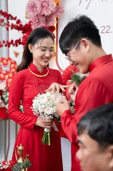 A joyful couple exchanges rings during a vibrant traditional Asian wedding ceremony.