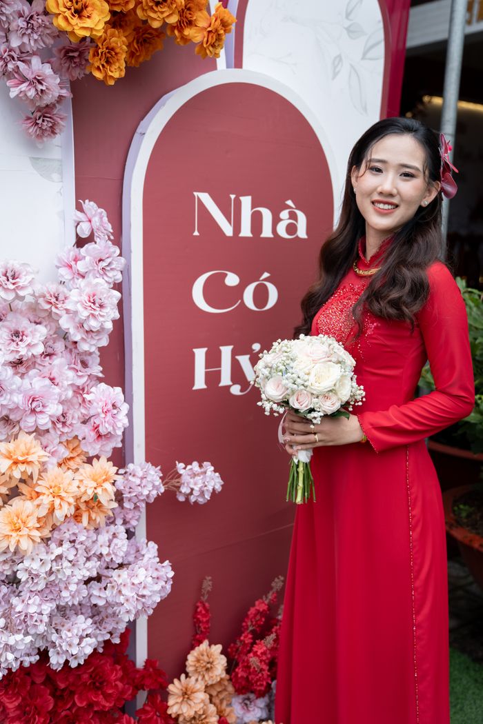 Cô dâu áo dài đỏ ôm hoa cưới trước bảng Nhà Có Hỷ