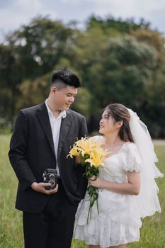 A couple in a classic wedding attire poses romantically outdoors with a vintage camera.