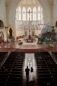 A couple walks down the aisle in a large, ornate church with elegant decor.